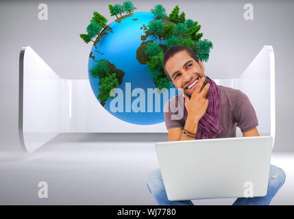 Composite image of thinking man sitting on floor using laptop and smiling Stock Photo