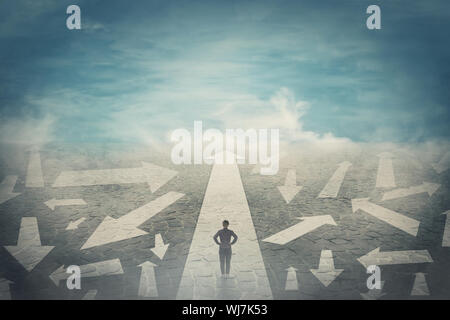 Doubtful person, hands on hips, choosing the way as multiple arrows on the road showing a mess of different directions. Choosing the correct pathway, Stock Photo