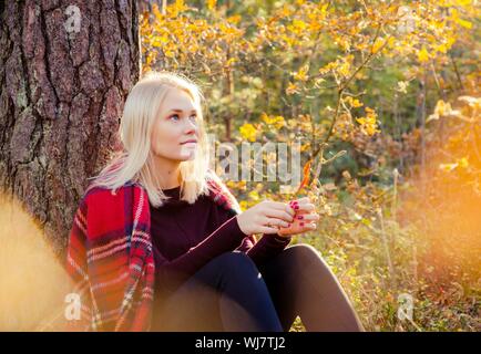 Portrait Of Young Woman Sitting In Forest During Autumn