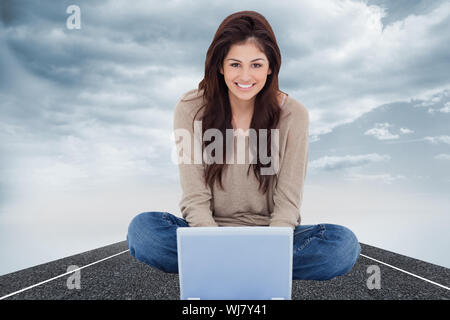 Composite image of a woman smiling as she looks forward in front of her laptop with crossed legs. Stock Photo