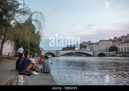 LYON, FRANCE - JULY 17, 2019: French people, mainly young men and women sitting on the riverbank of the Saone (quais) in the evening while people are Stock Photo