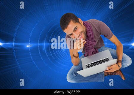 Composite image of thoughtful man sitting on floor using laptop and smiling at camera Stock Photo