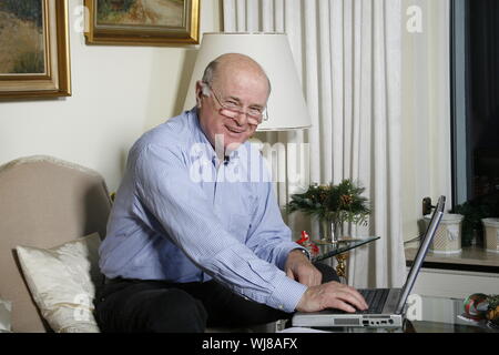 Ein freundlicher, positiver Senior zuhause telefoniert,mit Laptop Stock Photo