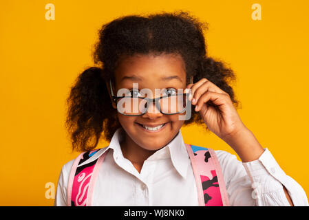 Black Elementary Schoolgirl Looking Over Glasses At Camera, Studio Shot Stock Photo