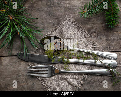 Vintage rustic cutlery set with country style napkin and Christmas decoration - fir tree brunch, cone on wooden background. Copy space, top view. Stock Photo