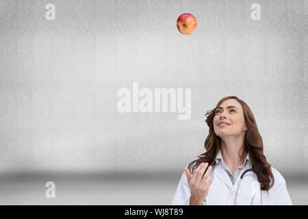Composite image of happy brunette doctor throwing apple Stock Photo
