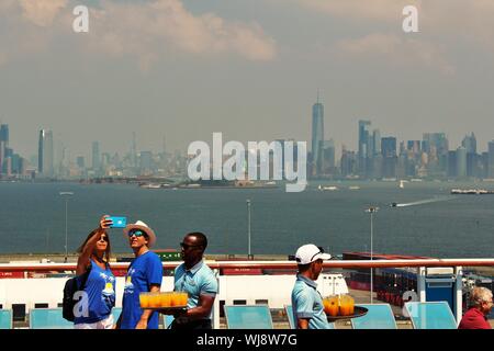 Passengers take a selfie in front of the New York skyline, whilst crew serve drinks on board the Anthem Of The Seas Royal Caribbean cruise ship. Stock Photo