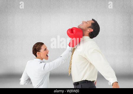 Composite image of businesswoman hitting a businessman with boxing gloves Stock Photo