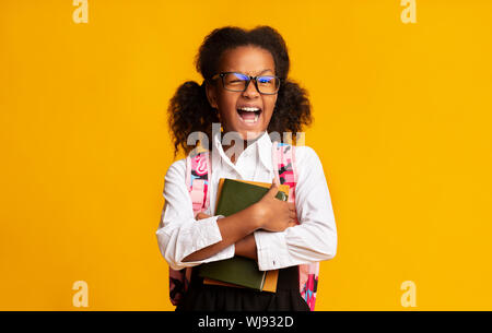 Afro Elementary Student Girl Winking At Camera Over Yellow Background Stock Photo
