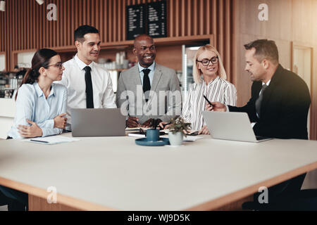 Diverse group of smiling businesspeople working on laptops and going over paperwork while standing around a table during an office meeting Stock Photo