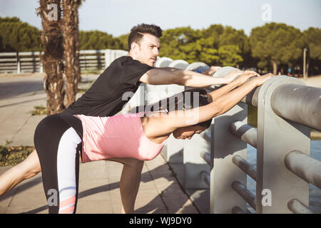 Caucasian Man and Latina Woman Stretch Muscles in Front of Lake After Running Stock Photo