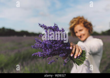 Close-up Of Woman Holding Lavender Flowers On Field Against Sky