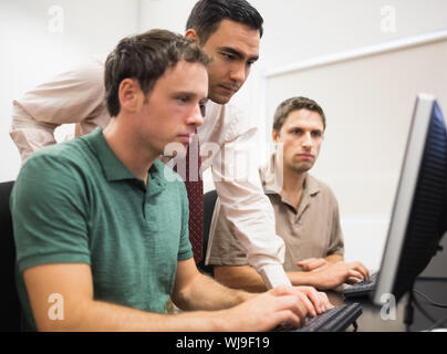 Concentrated teacher with mature students using computer in the computer room Stock Photo