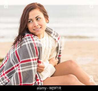 Beautiful young woman covering herself with blanket at the beach Stock Photo