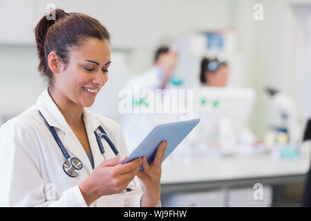 Close-up of a female doctor using tablet PC with colleagues in background at medical office Stock Photo