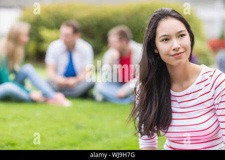 Smiling young college student with blurred friends sitting in the park Stock Photo