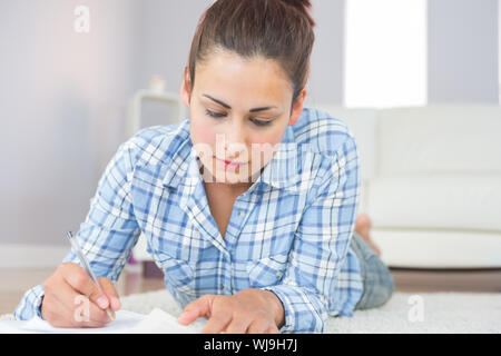 Young brunette student lying on the floor doing assignments in the living room Stock Photo