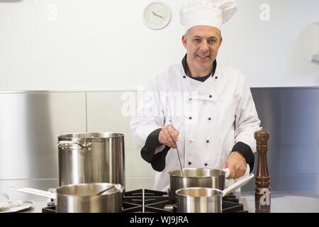 Smiling head chef holding ladle looking at camera in professional kitchen Stock Photo