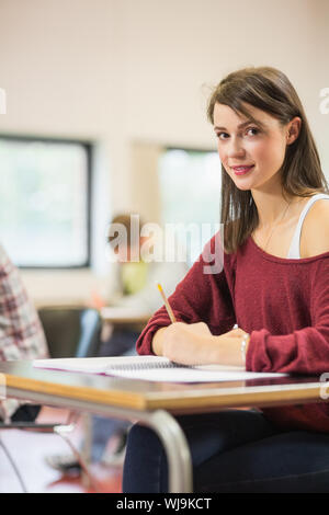 Portrait of a smiling female student with others writing notes in the classroom Stock Photo