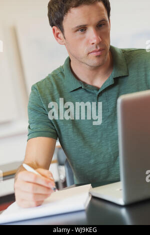 Focused handsome mature student using his notebook for learning while sitting in classroom Stock Photo