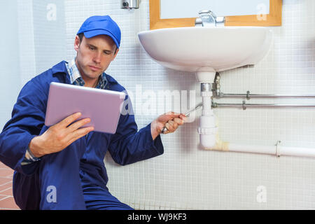 Serious plumber consulting tablet in public bathroom Stock Photo