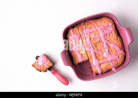 Pink brownie cake in the tray and a portion on white table. Above view of ruby chocolate dessert. Flat lay of pink dessert. Tasty pink chocolate food. Stock Photo
