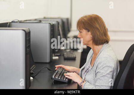Concentrated female mature student sitting in computer class working on computer Stock Photo