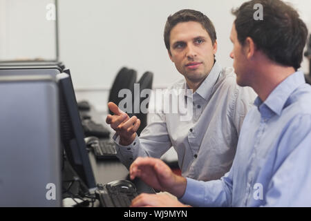 Two handsome men talking while sitting in computer class pointing at monitor Stock Photo