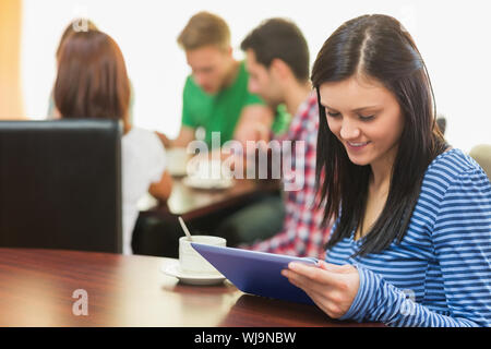 Smiling female with coffee using tablet PC and students around table in background at  the coffee shop Stock Photo