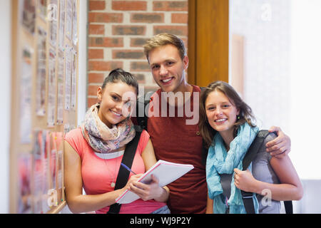 Three smiling students standing next to notice board in school Stock Photo