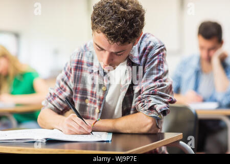 Young male student with others writing notes in the classroom Stock Photo