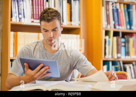 Attractive focused student using tablet and turning page in library Stock Photo