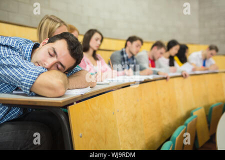 Male sleeping with students sitting in the college lecture hall Stock Photo