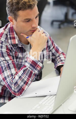 Handsome thoughtful student using computer taking notes in computer room at college Stock Photo