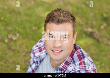 Handsome smiling student sitting on grass on campus at college Stock Photo