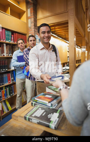 Attractive man handing a book to the female librarian in library Stock Photo