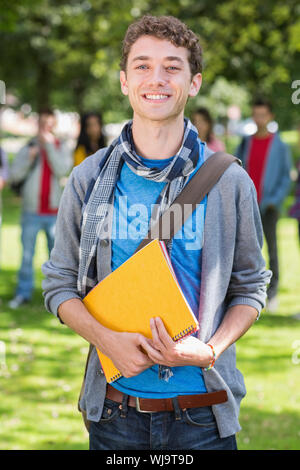 Portrait of college boy holding books with blurred students standing in the park Stock Photo