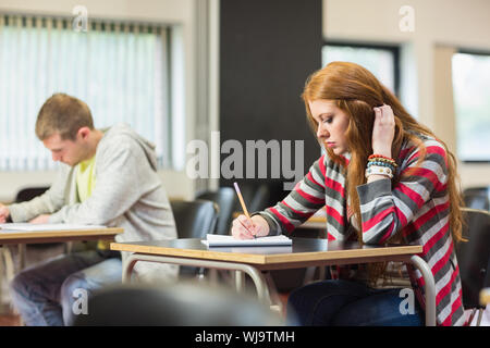 Young female student with others writing notes in the classroom Stock Photo
