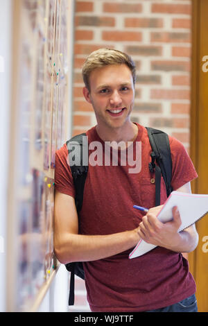 Handsome smiling student taking notes next to notice board in school Stock Photo