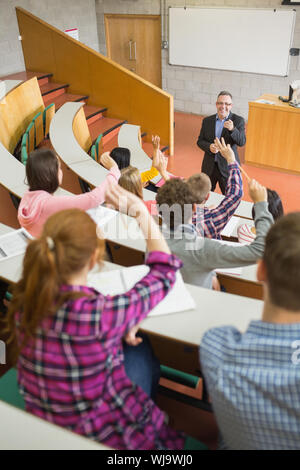 Rear view of students raising hands with a teacher in the college lecture hall Stock Photo