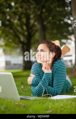 Thoughtful casual student lying on grass taking notes on campus at college Stock Photo