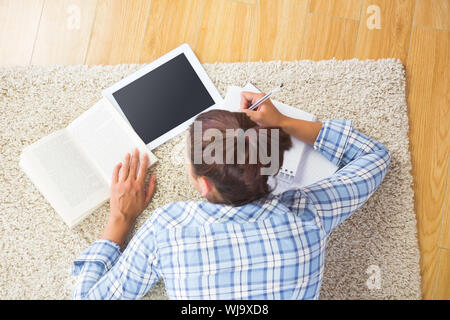 Brunette female student lying on the floor doing assignments using her tablet Stock Photo