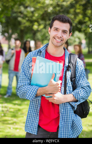 Portrait of college boy holding books with blurred students standing in the park Stock Photo