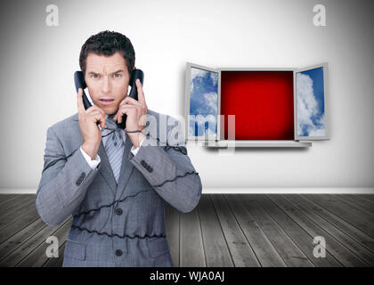 Angry businessman wrapped in cables phoning in front of open window Stock Photo