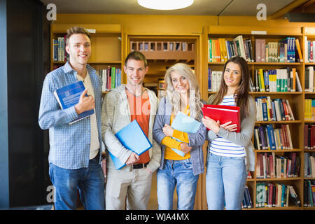 Group portrait of four students with folders standing against bookshelf in the college library Stock Photo