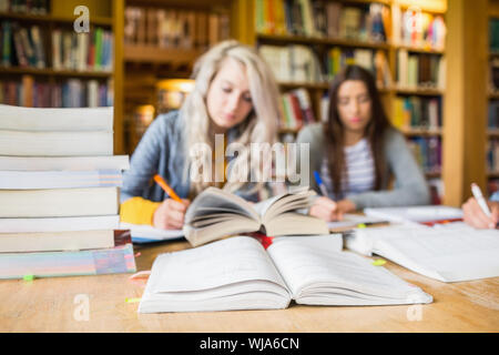 Two blurred students writing notes with stack of books at desk in the college library Stock Photo