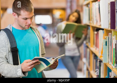 Two young students reading by bookshelf in the library Stock Photo