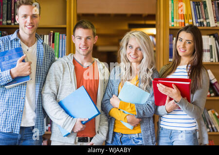 Group portrait of four students with folders standing against bookshelf in the college library Stock Photo