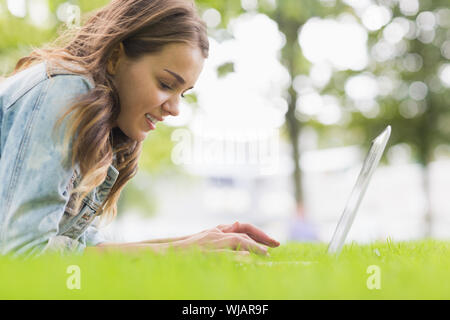 Happy student lying on the grass using her laptop Stock Photo