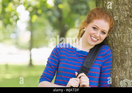Cheerful redhead student leaning against a tree Stock Photo